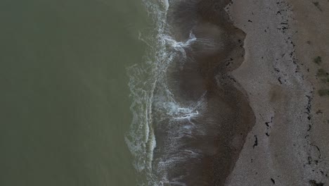overcast day on a uk shingle beach. gentle waves wash the shore. a simple, serene coastal scene from a top-down perspective, emphasizing the beach texture.