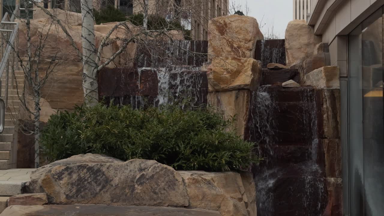 Camera pans down over waterfall as it vanishes behind large rock in foreground