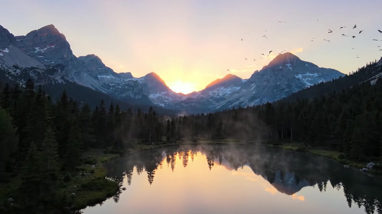 Un'Alba Serena in Montagna su Acque Calme: Assisti allo Splendore della Natura Mentre il Sole Sorge Dietro Cime Maestose, Illuminando un Lago Tranquillo Circondato da Foreste Rigogliose