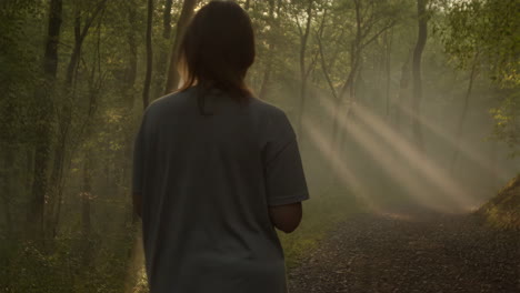Woman Walking Through a Misty Forest with Sunbeams