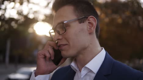 Caucasian-businessman-in-stylish-glasses-talking-on-the-mobile-phone-on-streets-of-business-district.-Young-confident-man-using