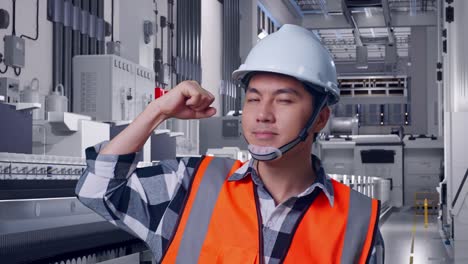 close up of asian male engineer with safety helmet flexing his bicep and smiling to camera while standing at pharmaceutical factory, vaccine production facility