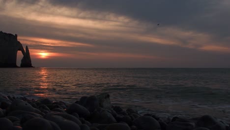 agua salpicando contra piedras y rocas del océano durante la hermosa puesta de sol y la silueta del acantilado en el fondo