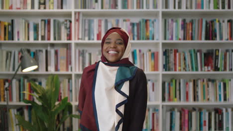 Retrato-De-Una-Joven-Y-Encantadora-Mujer-Afroamericana-Riéndose-Mirando-A-La-Cámara-Estudiante-Parada-En-La-Biblioteca