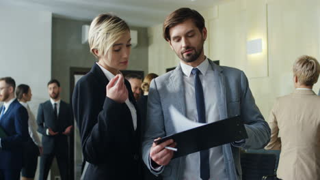 caucasian businesswoman and her male colleague talking and discussing documents and charts in the hall at a meeting