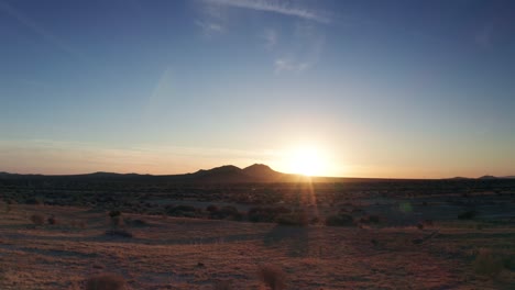 bright sun on horizon casting light rays over golden mojave desert, dolly left