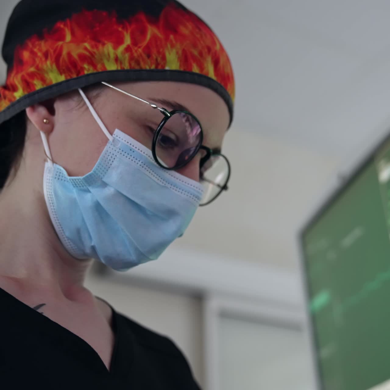 Dark-haired young female medic in black uniform, cap, mask and eyeglasses. Doctor looks at the screens of lung ventilation systems. Low angle view close up