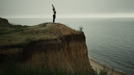 Mujer-Atlética-Parada-Enderezando-La-Colina-De-La-Playa-Estirando-Las-Manos-Hacia-El-Cielo-Gris.