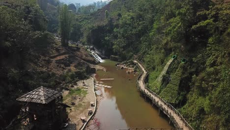 una toma aérea de un pequeño pueblo con un puente de madera y una pasarela a lo largo de un río marrón fangoso en sapa vietnam