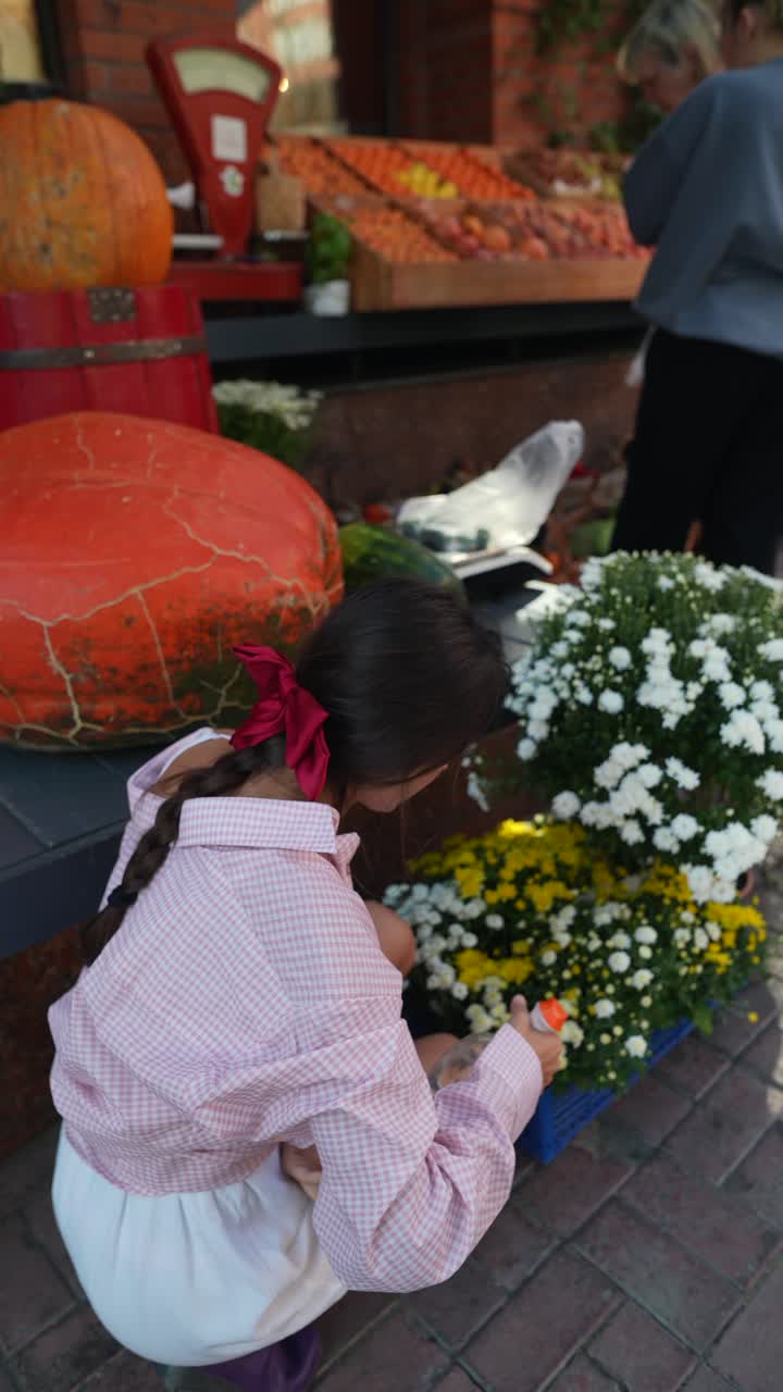 niña inspeccionando flores en un mercado con calabazas