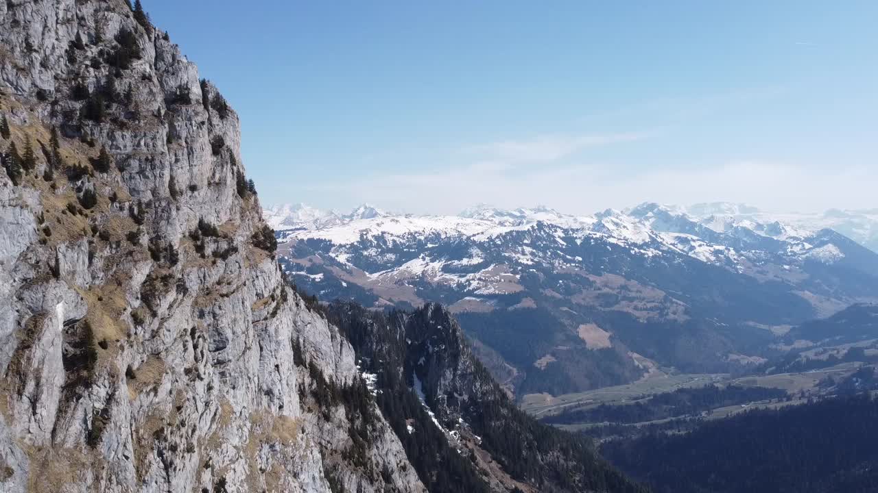 drone flies along steep mountain slopes with the stunning snowy swiss alps in the background in fine sunny weather