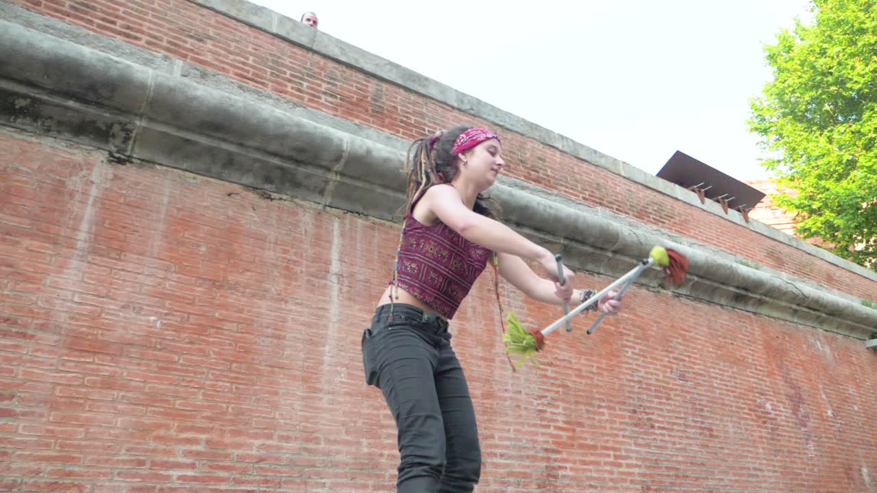 SlowMotion Low Angle of Girl with Dreadlocks Spinning Sticks as part of Circus Skills with Kick up