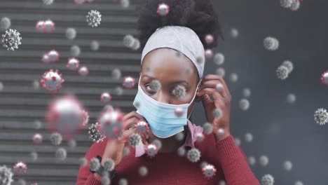 animation of covid 19 cells over african american woman wearing face mask