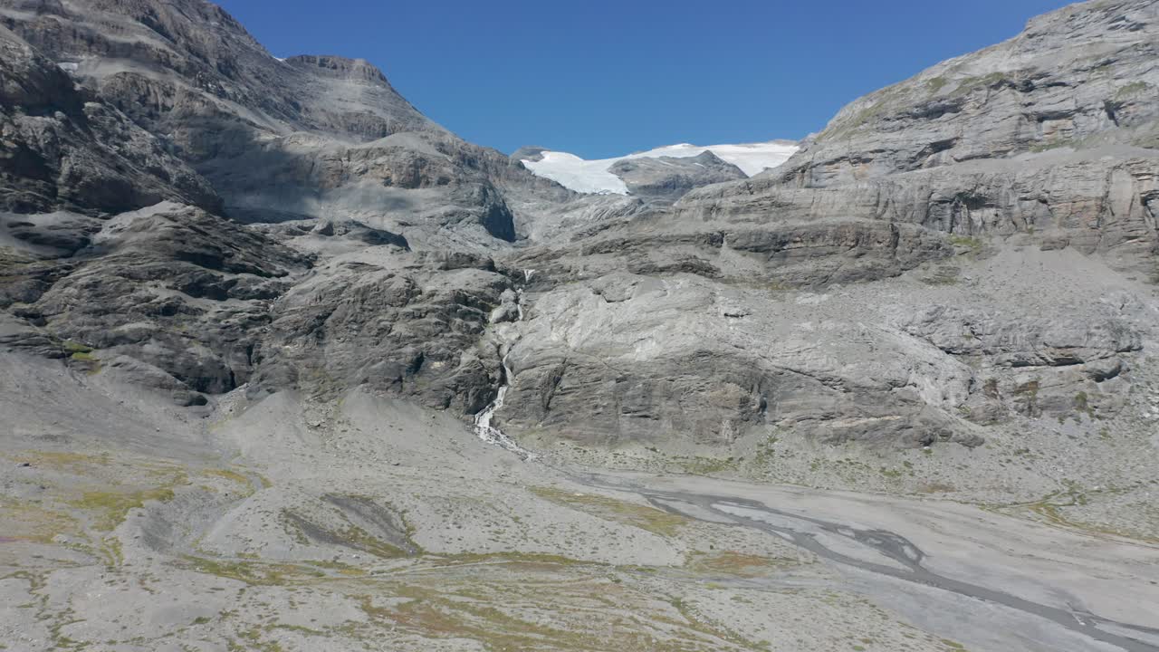 drone volando hacia una pequeña cascada que fluye a un lago seco en las montañas