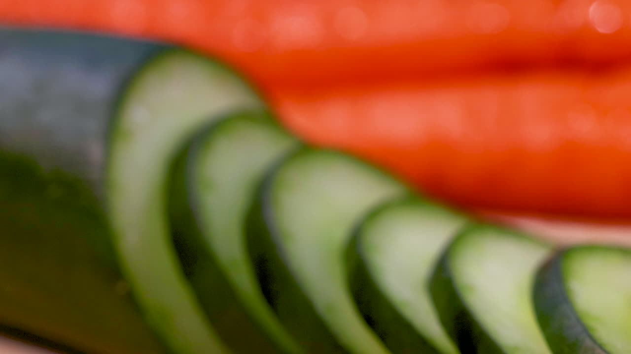 близкое видео, демонстрирующее свежие нарезанные огурцы и морковь, подчеркивая яркие цвета и текстуры в кухонной обстановке