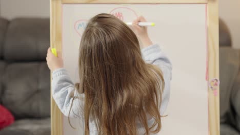 a young girl drawing on an easel with markers