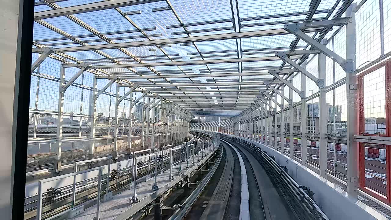 A train navigates through a modern urban setting in Tokyo, showcasing dynamic movement and architectural structures under clear daylight