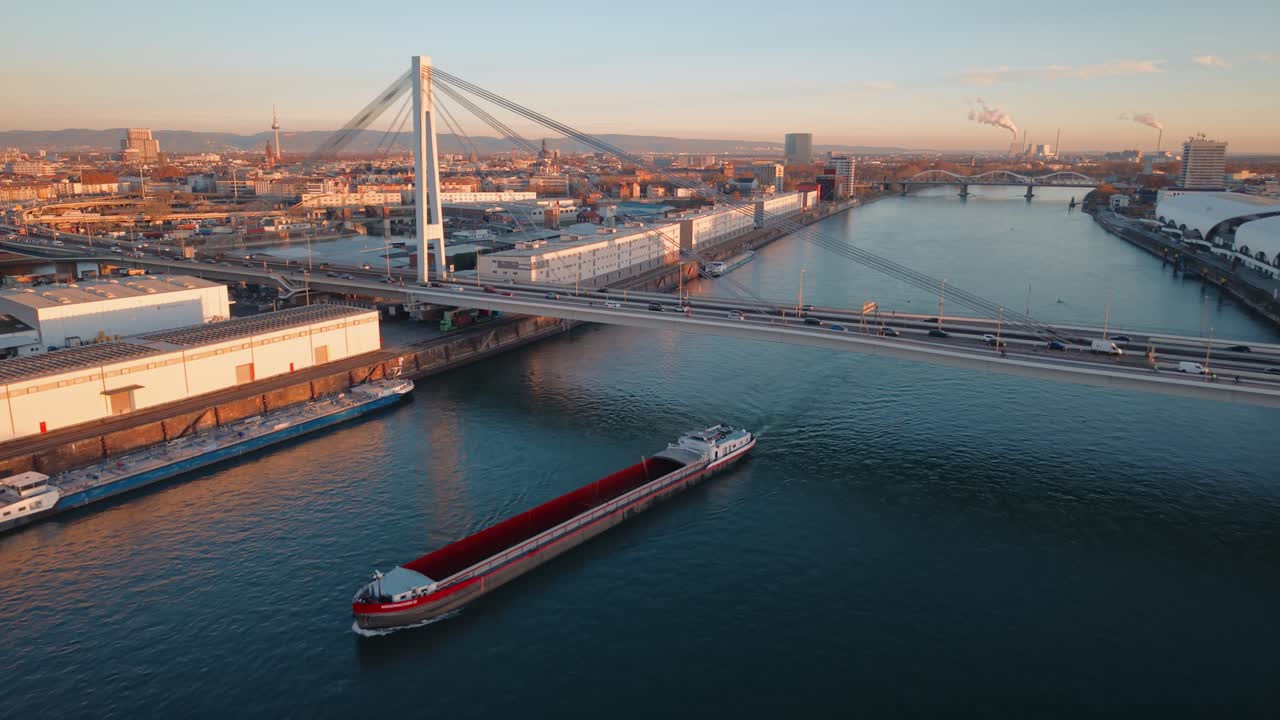 Golden Hour Aerial of Mannheim Rhein Bridge: Barge Navigating Industrial Harbor and City Skyline Traffic at Sunset, Germany