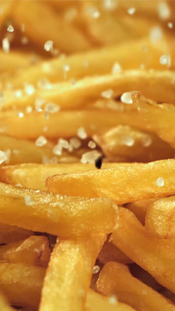 Primer plano a cámara lenta de sal cayendo sobre patatas fritas doradas