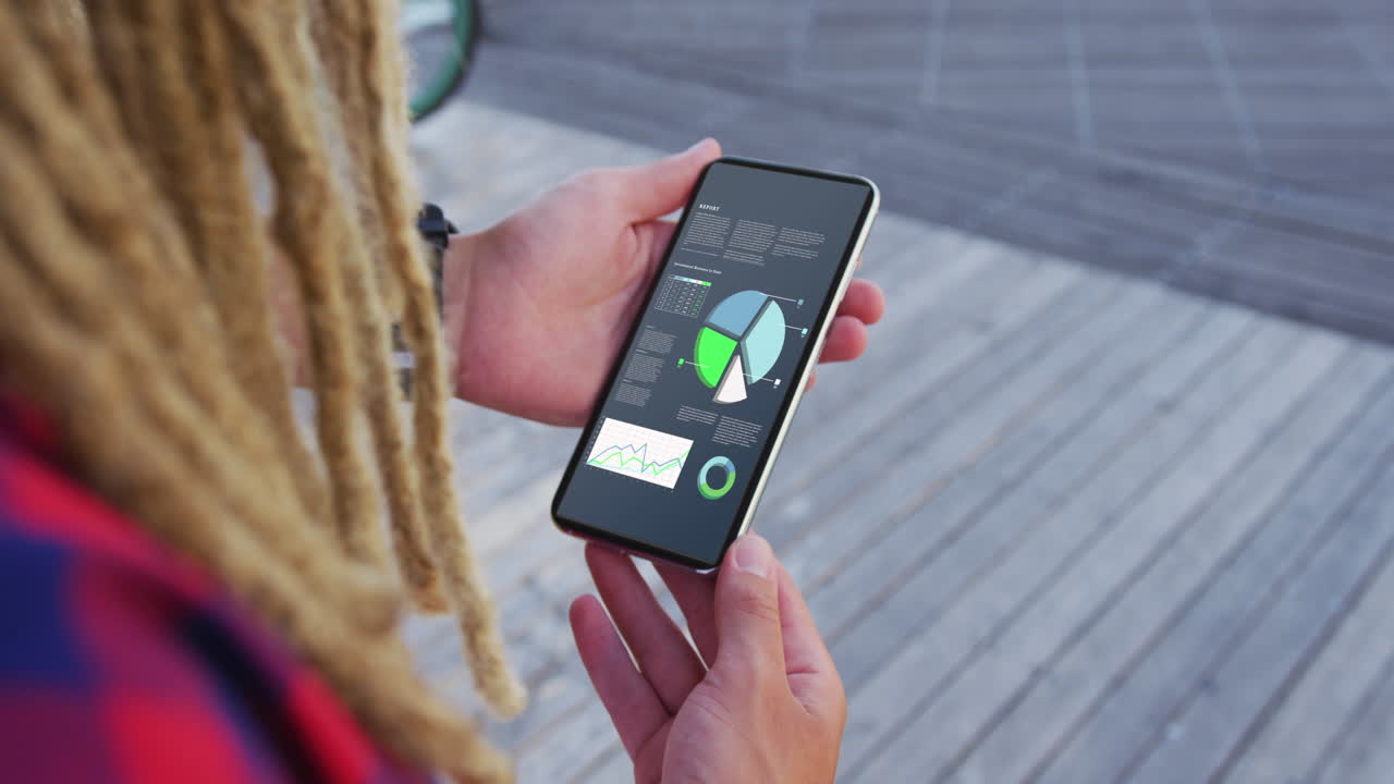 스크린에 통계를 가진 스마트 폰을 사용하는 dreadlocks를 가진 백인 남자의 손