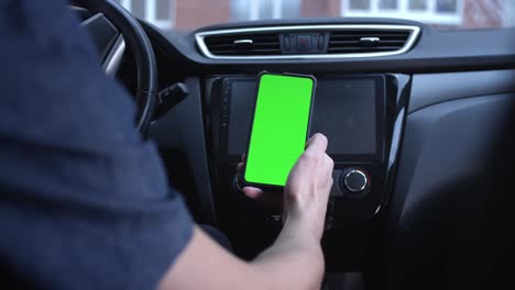 un conductor masculino usa un teléfono inteligente verticalmente con una pantalla verde, sostiene un teléfono en la mano. maqueta para un navegador o aplicación de carretera. desliza a la izquierda y a la derecha. aplicación de citas.