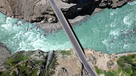 drone shot of turquoise blue water river flowing under a bridge in karakoram mountain range along karakoram highway, downward angle