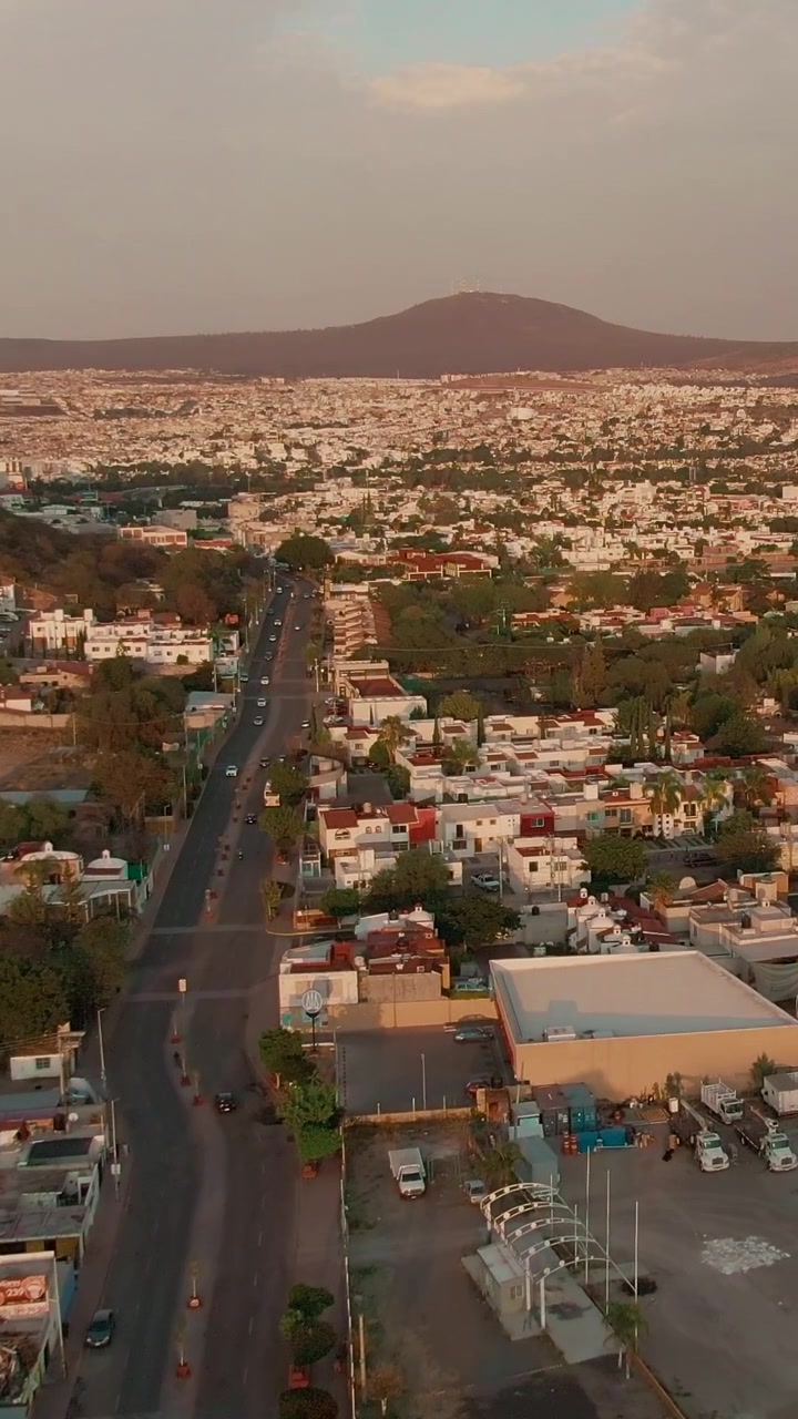Strada rettilinea che attraversa quartieri residenziali e conduce verso colline distanti sotto la calda luce del tramonto a Santiago de Querétaro. Vista aerea verticale