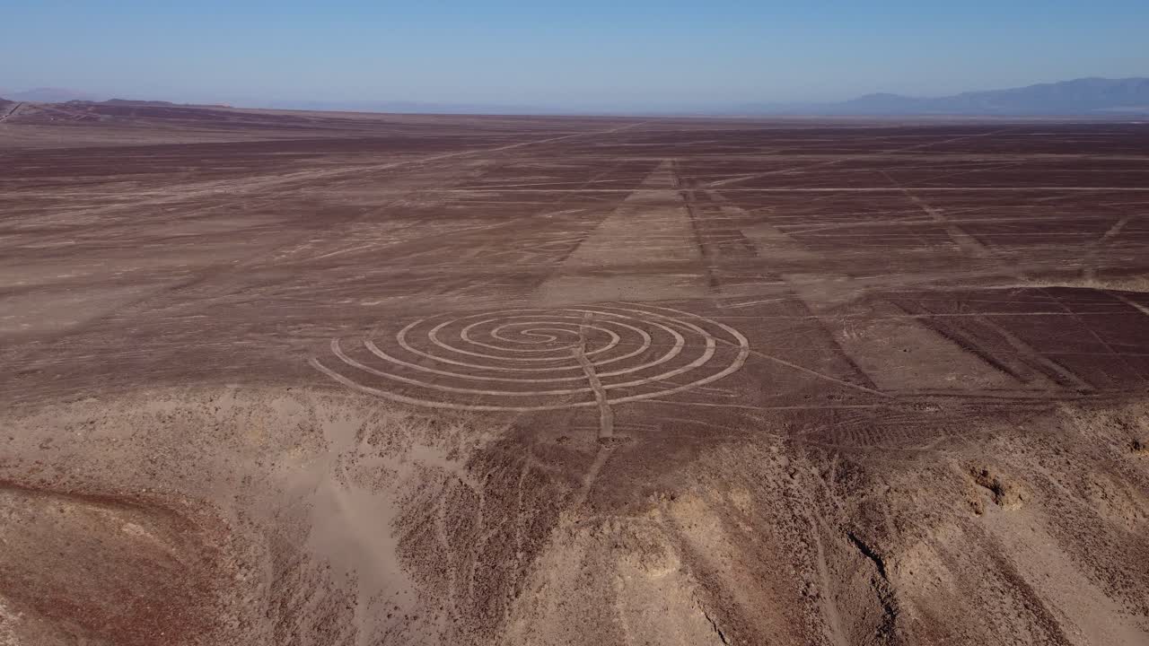 Ancient spiral and long geoglyphs on top of a desert plateau, part of the famous Nazca Lines. Drone orbits around while tilting camera up. Located in Nazca, Peru
