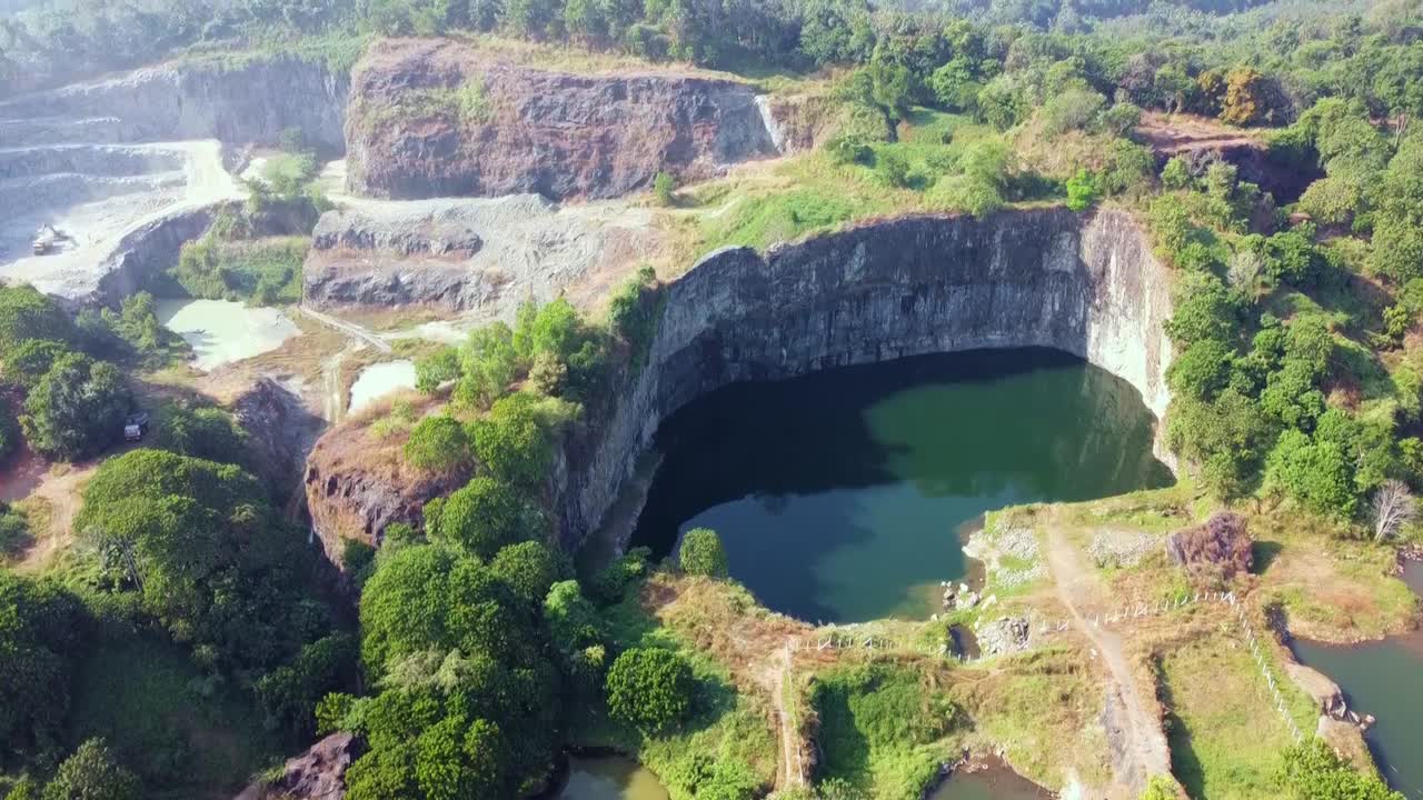 Drone view of a rock quarry in India with terraced excavation, trucks, water pits and lush green surroundings. Ideal for themes on mining, geology, terrain, environment, industry, nature and earth