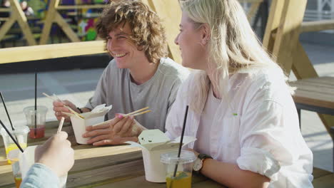 group of  friends chatting, while sitting around an outdoor table and eating street food