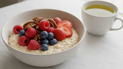 a delicious bowl of oatmeal topped with fresh berries and pecans accompanied by a cup of herbal tea, perfect for a healthy breakfast