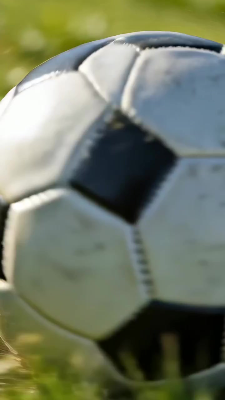 Video vertical: Balón de fútbol desgastado rodando, entrando por la derecha, girando sobre el césped y frenando en el suelo.