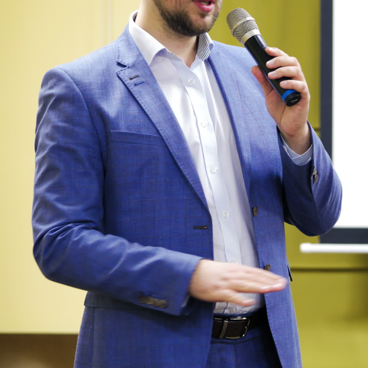 Close-up of a man speaker in blue jacket talking into the microphone. Male educator leading a seminar in a conference hall.
