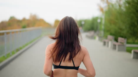 close-up back view of fair woman jogging in park with a clear background of green trees and benches, capturing active lifestyle, fitness, and energy in outdoor exercise