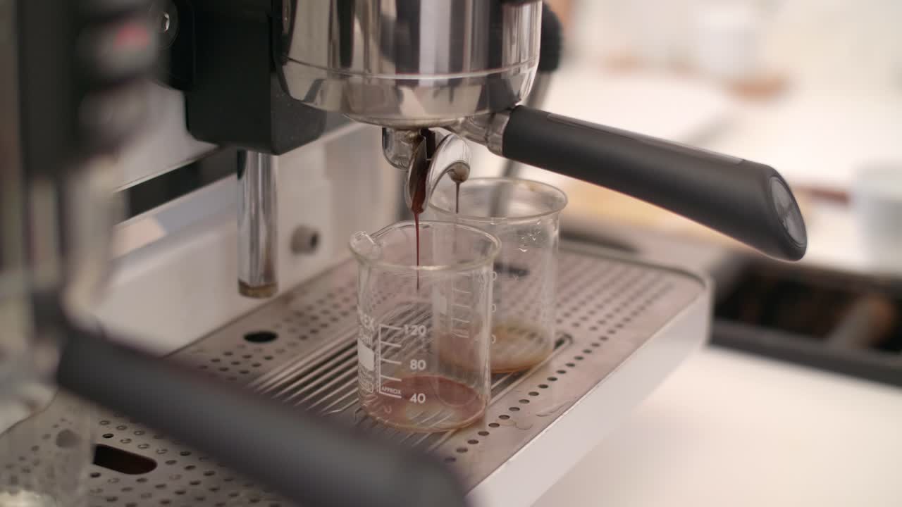 두 개의 측정 컵은 포타 필터를 통해 떨어지는 커피로 가득 차 있습니다.