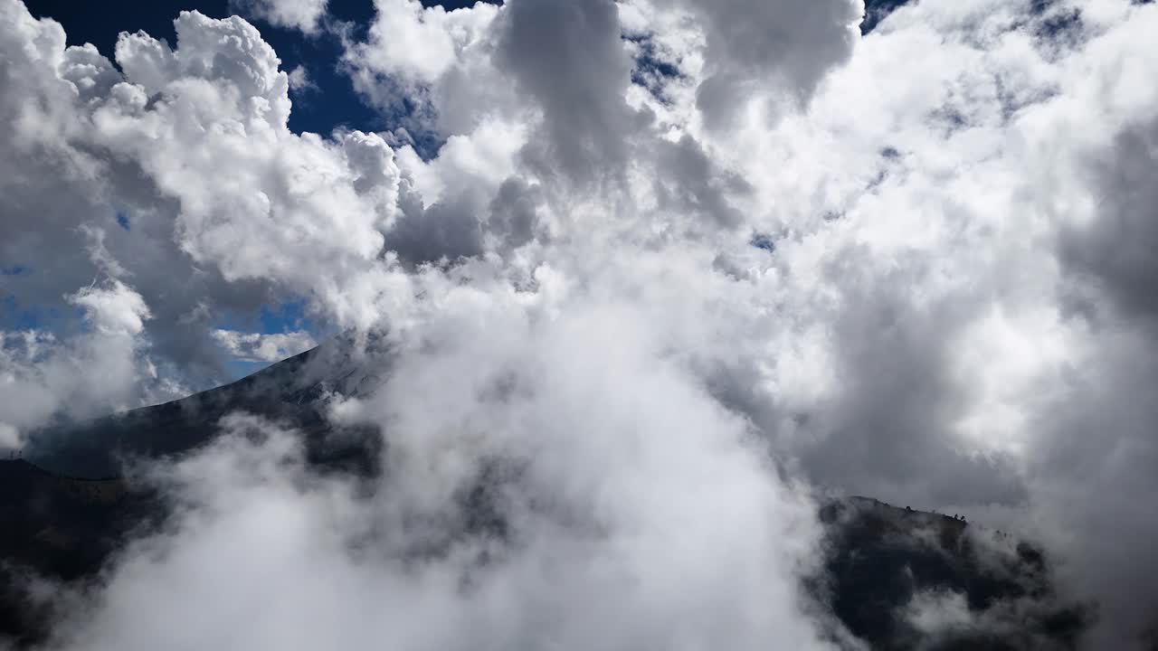 Aerial drone shot capturing the Popocatépetl volcano on a cloudy morning, ending by navigating through the cloud bank in Mexico
