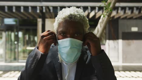 portrait d'un homme âgé afro-américain en masque portant des écouteurs dans un parc d'entreprise