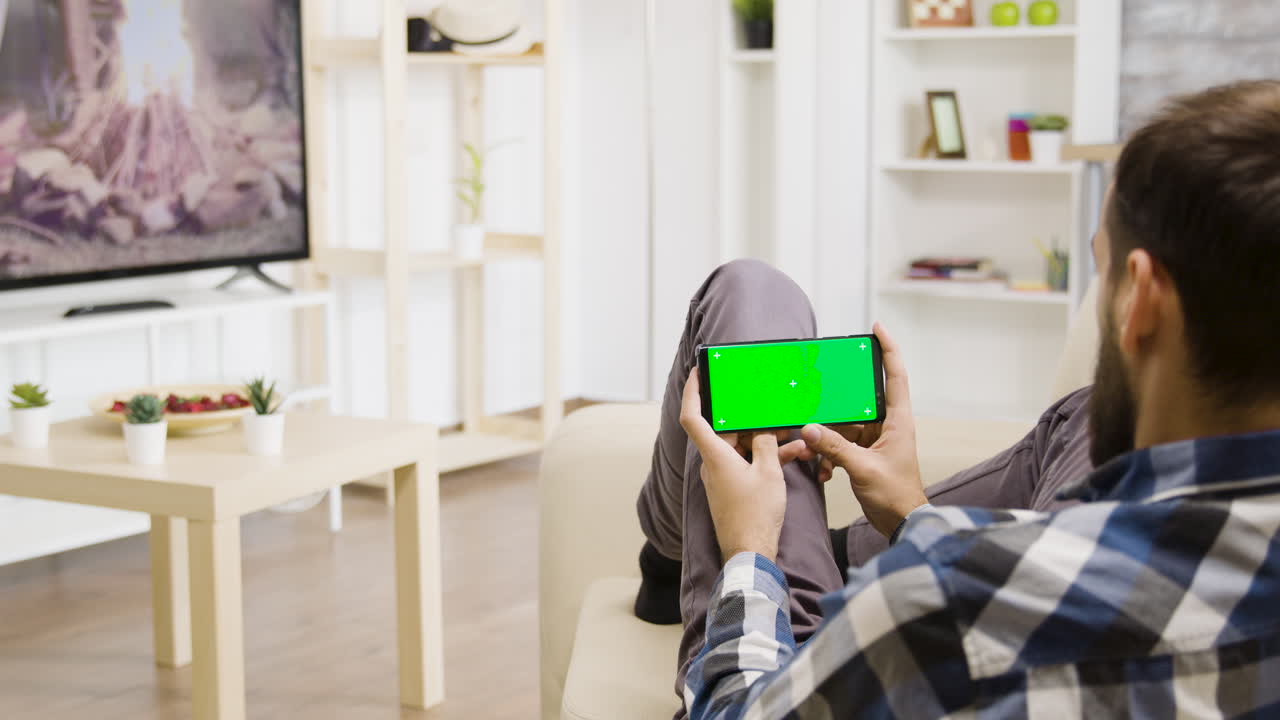 Man using smartphone with green screen in living room