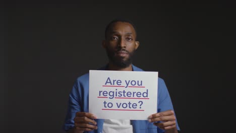 portrait of man holding are you registered to vote sign in election against black background