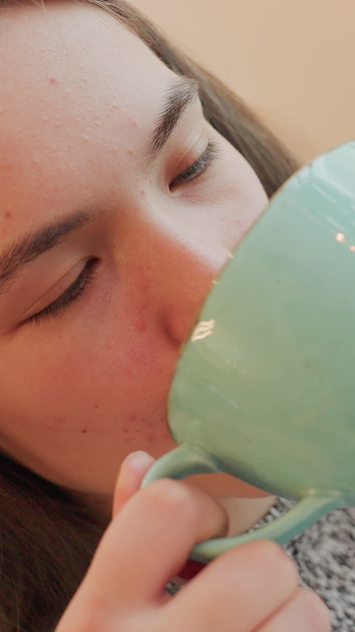 라떼를 음미하며 사색에 잠긴 채 조용한 실내에서, 젊은 여성이 민트색 머그잔을 안정된 손으로 들어 올리고, 손가락으로 손잡이를 잡고, 눈을 감았다가 부드럽게 뜨며, 거품과 세라믹 디테일, 명상적인 순간을 보여줘요.