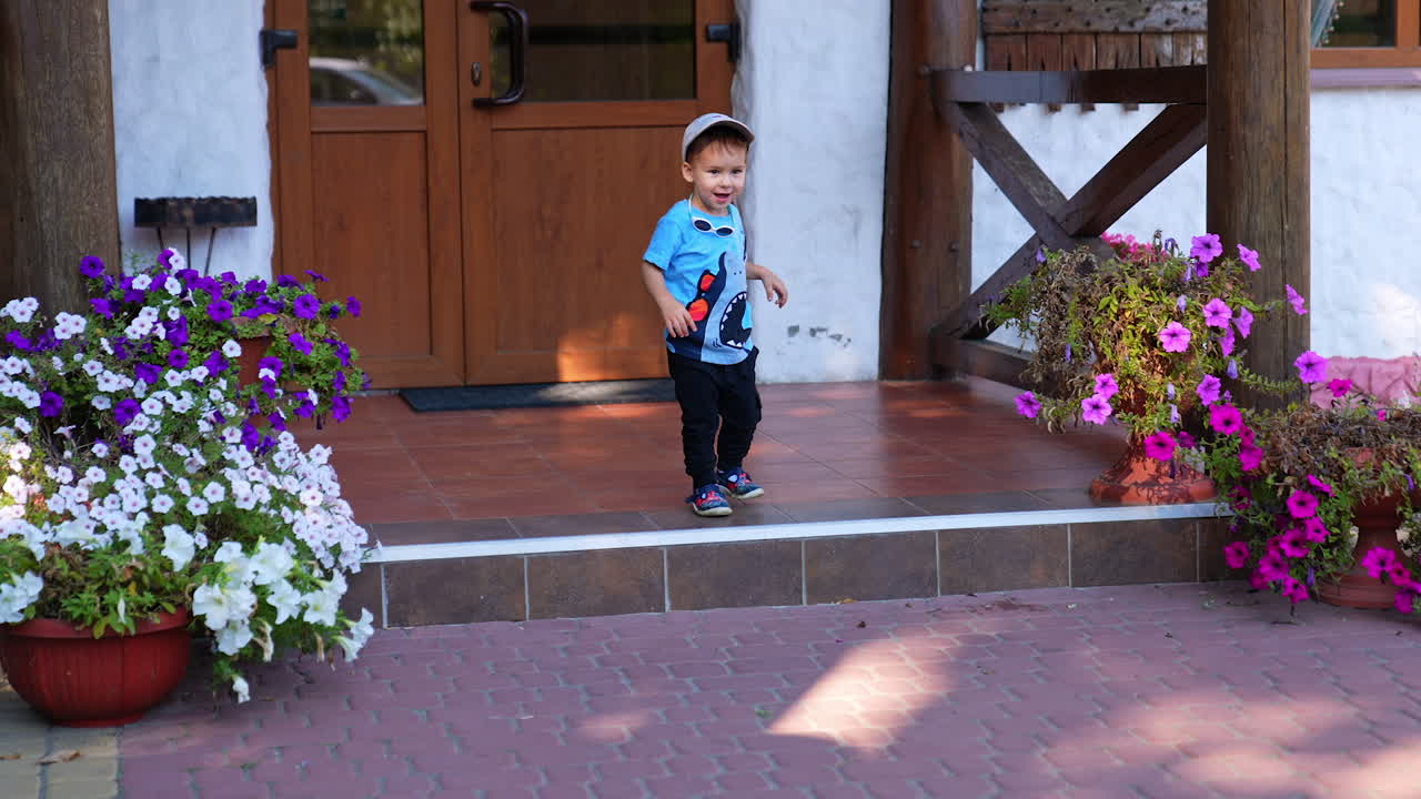 Adorable baby boy steps on the house porch with beautiful flowers on. Happy energetic baby jumping off the stair.