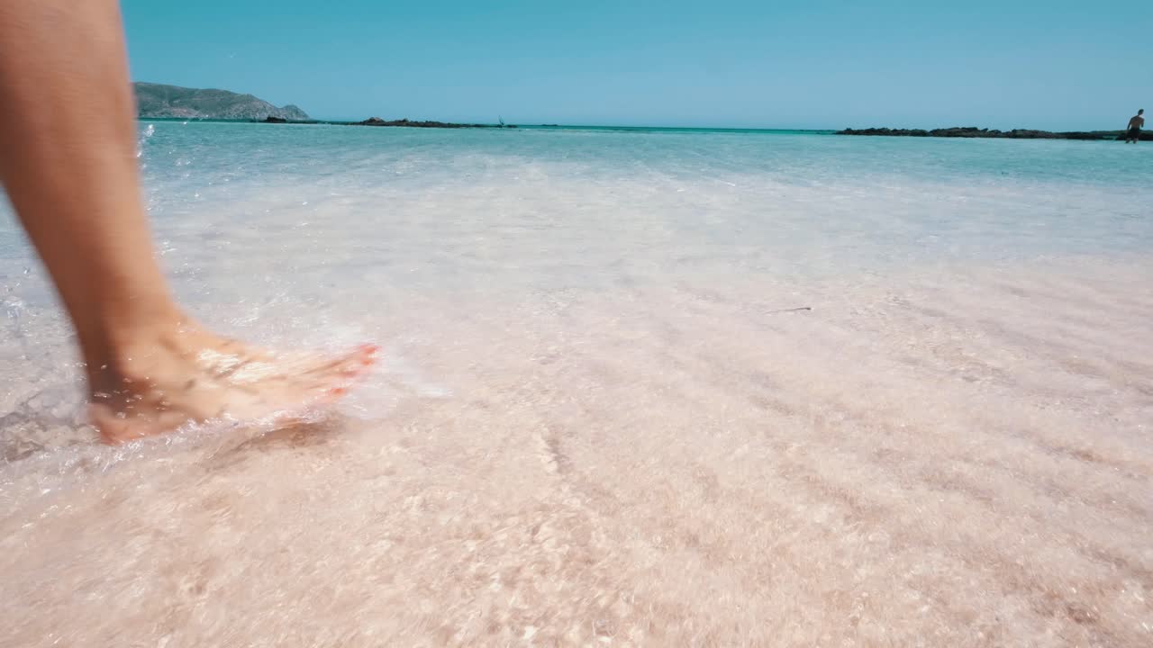 niña caminando en la playa rosa, pies en el agua