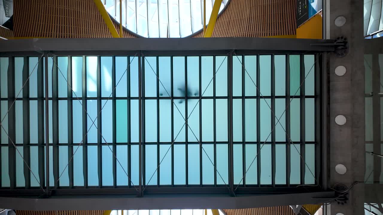 Static shot of a translucent tempered glass pedestrian bridge as travelers with luggage cross inside Adolfo Suárez Madrid-Barajas International Airport, Spain