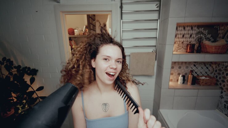 chica alegre bailando y cantando con secador de pelo y peine en el baño