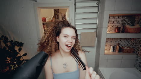 chica alegre bailando y cantando con secador de pelo y peine en el baño
