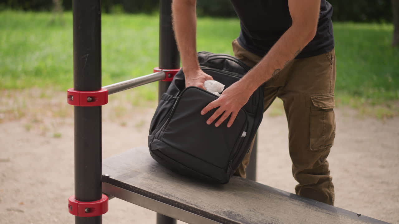Man Arranging Backpack Thoughtfully Outdoors, Systematic Arrangement Of Equipment Before Training In Park Environment, Careful Organization Of Gear By Man Before Engaging In Outdoor Training Session