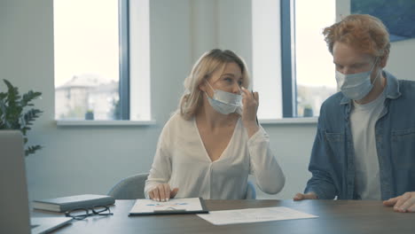 Junge-Geschäftsfrau-Und-Mann-Mit-Gesichtsmaske-Machen-Ellbogenstöße-Und-Besprechen-Die-Arbeit-Im-Büro