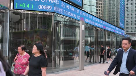 people move past a dynamic screen at exchange square, home to the hong kong stock exchange (hkex), displaying negative stock ticker symbols in the heart of hong kong's financial district.