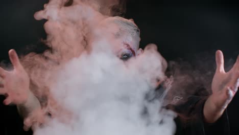 hombre siniestro con horrible y aterrador maquillaje de halloween zombi en disfraz sopla humo de la nariz y la boca