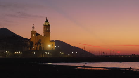 Rote-Küste-Bei-Sonnenuntergang-In-Der-Dämmerung-Mit-Einer-Kirchensilhouette-Aus-Hügeln-Und-Fliegenden-Vögeln